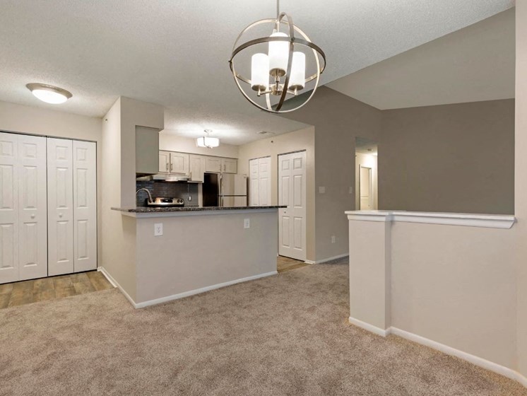 Carpeted Living Room Next to Kitchen with Breakfast Bar White Cabinets and Stainless Steel Appliances